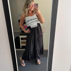 Svart maxiklänning med virkad topp - Supersnygg långklänning med svart kjol och vit virkad topp. Smala axelband och flowy passform, perfekt för sommarens alla tillfällen. Den virkade delen har coola håldetaljer och ger en bohemisk vibe. Ingen synlig logga.Helt ny