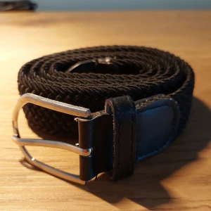 Svart flätat bälte med skinn och metallspänne - Snyggt svart bälte med flätad design och detaljer i svart skinn vid spännet och änden. Har den I storlekarna 90 100 105 110cm 