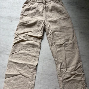 Beiga linnebyxor  - Snygga och avslappnade beiga linnebyxor med resår och snörning i midjan. Byxorna har raka ben och sidofickor, perfekta för en chill och luftig stil under varmare dagar. Byxorna är från Lindex och är i storlek 146 men det är hyfsat stora.