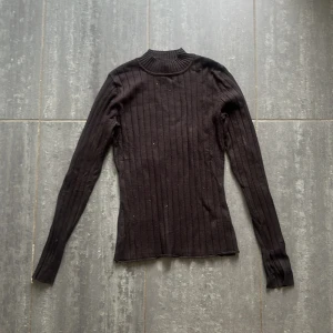 Svart ribbad polotröja från H&M - Svart ribbad polotröja från H&M i storlek M. Tröjan har lång ärm, smal passform och högre krage. Perfekt att styla med jeans eller kjol för en clean look. 