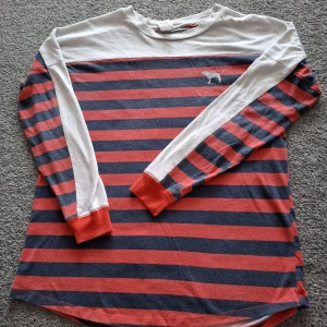 Randig långärmad tröja PINK 86 - Snygg långärmad tröja från PINK med marinblå och röda ränder, vita partier upptill och på ärmarna samt röda muddar. Stor silverglittrig PINK-text och siffran 86 på ryggen. Mjuk bomullskänsla och sportig college-vibe.