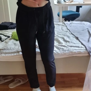 Svarta mjukisbyxor med snörning - Svarta mjukisbyxor med dragsko i midjan och fickor på sidorna. Byxorna har en relaxed fit och är perfekta för chill dagar. Materialet är mjukt och bekvämt, och modellen är något avsmalnande nertill.