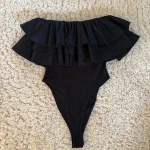 Svart volangbody från Zara - Säljer en supersnygg svart body från Zara med breda volanger över axlarna💕