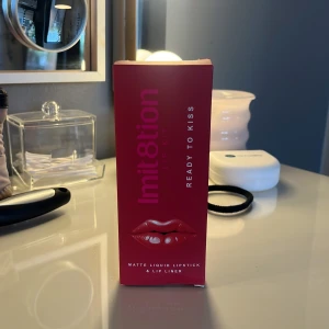 Lip kit - Säljer ett Imit8tion Lip Kit i färgen Ready To Kiss. Kitet innehåller ett matt flytande läppstift (5,5 ml) och en matchande läppenna (1 g), båda i en intensiv röd nyans. Förpackningarna är stilrena i vitt och rött, perfekt för att skapa skarpa och fylliga läppar. Ingen av dem är använda, inte testade heller. Dem skickas i orginal förpackningen men mer säkert. Skriv för fler frågor!