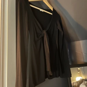 Svart knytblus från Design by Si - Svart blus från Design by Si i storlek XS/S. Modellen har långa ärmar och en snygg knytning framtill som ger en cool och trendig look. Perfekt att styla med jeans eller kjol för en chic outfit.