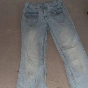 Ljusblå jeans med fickdetaljer - Säljer ett par ljusblå jeans med raka ben och stora fickor framtill med lock och knapp. Jeansen har klassisk passform och är tillverkade i denim. Perfekta för en chill och avslappnad stil.