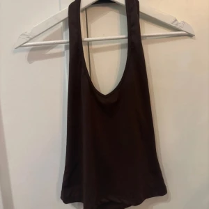 Brun ärmlös linnetopp med djup rygg - Säljer en brun ärmlös linnetopp med djup urringning både fram och bak. Toppen har en tajt passform och är tillverkad i ett mjukt, lätt material som känns skönt mot huden. Perfekt för dig som gillar en enkel men snygg stil.