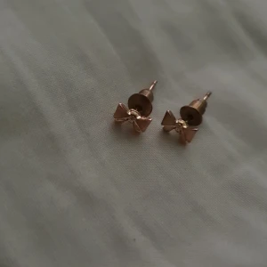 Guldiga örhängen med rosett - Supersöta små örhängen i guld med rosettform. Perfekta för dig som gillar en söt och stilren look. De är små och diskreta men ändå unika med sin fina rosettdetalj.