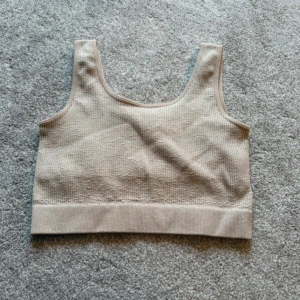 Beige ribbad sporttopp från Bik Bok - Säljer en beige ribbad sport topp från Bik Bok i storlek XS/S. Toppen har en croppad passform, breda axelband och är tillverkad i ett stretchigt material med struktur. 