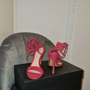 Rosa klackade sandaler med snörning - Snygga rosa sandaler från NA-KD med hög klack och öppen tå. Skorna har en unik design med dekorativa snörade detaljer runt vristen och är tillverkade i mocka. Perfekta för dig som vill sticka ut med en färgstark och trendig look.