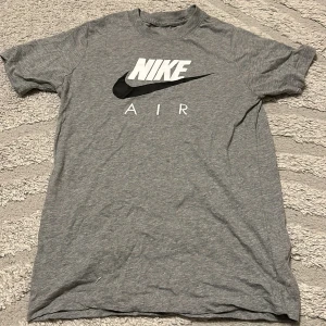 Grå Nike Air t-shirt - Snygg grå t-shirt från Nike med klassisk Air-logga i vitt och svart på bröstet. T-shirten har rund hals och korta ärmar, perfekt för en sportig och avslappnad stil.