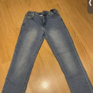 Blå jeans från D.M.D i rak modell - Snygga blå jeans från D.M.D By denim day i storlek 158. Klassisk femficksmodell med raka ben och normal passform. Jeansen har ljus tvätt och subtila slitningar för en avslappnad look. Perfekta till vardags med t-shirt eller hoodie.