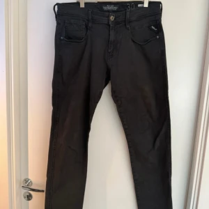Svarta Replay Anbass jeans, stl 30/32 - Säljer ett par svarta Replay Anbass jeans i storlek 30/32. Klassisk femficksmodell med dragkedjegylf och raka ben. Jeansen har en stilren look och är tillverkade i mjuk bomullsblandning för skön passform.