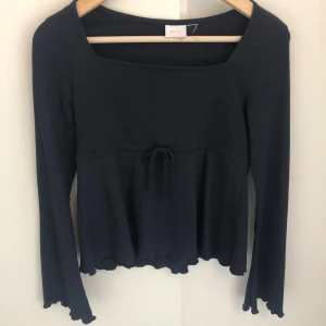 Blus från Gina Tricot  - Supersöt mörkblå långärmad topp från Gina Tricot med fyrkantig ringning och knyt i midjan. Perfekt till jeans eller kjol!