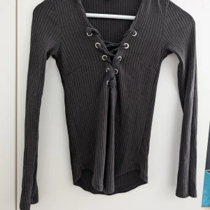 Svart ribbad tröja med snörning Gina Tricot - Svart långärmad tröja från Gina Tricot i ribbat material. Snygg snörning framtill med metallöljetter ger en edgy vibe. Tröjan har en figurnära passform och är perfekt att styla med jeans eller kjol. Superenkel att matcha och passar året runt. Har katter i hemmet och där av kan ha katthår på sig annars inget fel