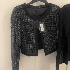 Rutig svartvit kavaj från Stockh LM - Snygg svartvit rutig kavaj från Stockh LM med rundad halsringning och croppad passform. Jackan har långa ärmar och är tillverkad i ett mjukt tyg med diskret struktur. Perfekt för dig som vill ha en stilren och trendig look.