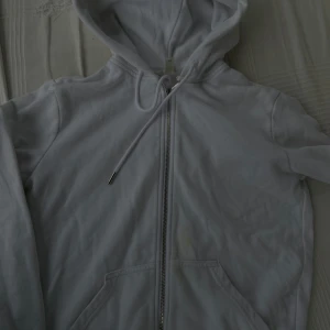 Vit hoodie med dragkedja XS - Vit hoodie i storlek XS med hel dragkedja framtill och snörning i huvan. Tröjan har kängurufickor och är tillverkad i mjuk bomullsmix. Perfekt för chill dagar eller när du vill ha en enkel och clean look. Säljer den billigt eftersom den har lite fläckar ska försöka få bort dem mer.