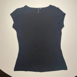 Svart ribbad topp Black Label XS - En svart, ribbad topp från The Black Label Collection i storlek XS. Modellen är figurnära med korta ärmar och rund halsringning. 