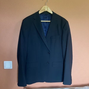 Svart kavaj These Glory Days - Stilren svart kavaj från These Glory Days med klassisk passform och två knappar framtill. Fodrad med mörkblått, glansigt innerfoder. 