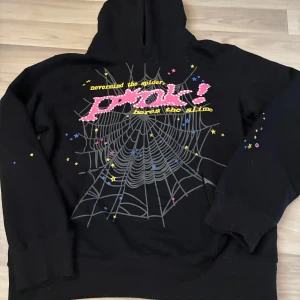 Svart hoodie med spindelnät och stjärnor - Svart hoodie med stor spindelnätsgrafik och texten 'nevermind the spiders, here's the slime' i rosa och gult framtill. Färgade stjärnor i blått och gult på ärmar och rygg, samt gul stjärnlogga bak. Mjuk bomullskänsla och huva.