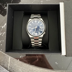 Citizen Tsuyosa - Citizen automatisk klocka med stilren blå urtavla och datumvisning. Boetten och länken är i blankt silverfärgat stål, vilket ger en klassisk och modern look. Helt ny, suttit på handleden i nån sekund.