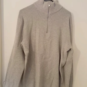 Grå stickad half zip från Jack & Jones - Snygg grå stickad tröja från Jack & Jones med hög krage och half zip-dragkedja. Perfekt för lager-på-lager och enkel att matcha med jeans eller chinos. Mjuk och skön känsla, passar dig som gillar stilren och clean look. Oanvänd 