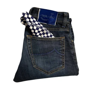 Jacob Cohën mörkblå jeans straight fit - Mörkblå jeans från Jacob Cohën med klassisk femficksdesign, raka ben och snygga kontrastsömmar. Jeansen har en blå patch med logga bak och levereras med en schackmönstrad scarf i bakfickan. Stängs med knappar i guldton. Perfekta för en stilren look.