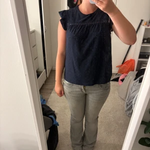 Mörkblå blus med volangärm från SHEIN - Supersöt mörkblå blus från SHEIN med broderade detaljer och små hålmönster. Blusen har volangärmar och en lös passform som ger en chill vibe. Perfekt till jeans eller kjol för en snygg look. Rund halsringning och ärmlös design. Pris kan diskuteras