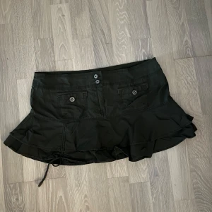 Grön y2k volangkjol  - Supersnygg grön kortkjol med volangkant och coola fickor både fram och bak. Kjolen har knappar framtill och en dragsko längst ner för extra detalj. Perfekt för dig som gillar en edgy och trendig stil. Från Soul Cal