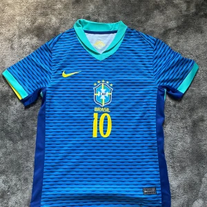 Blå Brasilien Neymar 10 fotbollströja Nike - Säljer en blå Brasilien fotbollströja med Neymar JR och nummer 10 på ryggen. Tröjan har korta ärmar, vågigt randigt mönster, gula detaljer och turkos krage. Tillverkad i lätt Dri-FIT material som andas. Perfekt för dig som älskar fotboll och Brasilien.