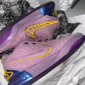 Nike LeBron XXI Violet Dust/Gold - Nike LeBron XXI sneakers i färgen Violet Dust/University Gold.                         SKORNA SAKNAR SNÖRE I HÖGER SKO!!!             Skorna har lila mockaöverdel, gula broderade detaljer och metallicblå häl. Snygg lila sula med unikt mönster och tydlig LeBron-logga. Perfekta för dig som vill sticka ut på basketplanen.