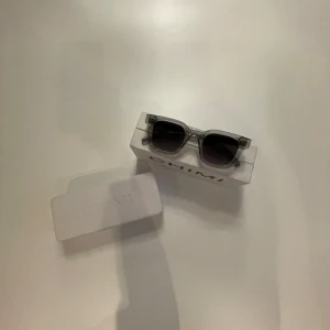 Grå transparenta solglasögon CHIMI - Snygga solglasögon från CHIMI i transparent grå plast med mörka glas. Rektangulär form och stilren design, perfekt för dig som gillar en modern och clean look. Märket syns tydligt på båda skalmarna.