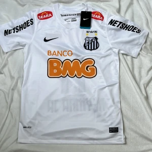 Helt ny vit Santos Neymar Jr fotbollströja från Nike - Santos officiella matchtröja i vitt med svarta detaljer, Neymar Jr och nummer 11 på ryggen. Broderat klubbmärke, sponsorer och Nike-logga. Lätt och ventilerande material, perfekt för fotbollsplanen.