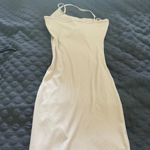 Beige ribbad klänning med asymmetrisk axel - Säljer en beige ribbad klänning med smala axelband och asymmetrisk axel. Klänningen är figurnära och har en mjuk, stretchig känsla. Köpt i Spanien och har ser för ingen etikett.
