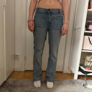 Blå bootcut jeansbyxor - Säljer ett par klassiska blå jeansbyxor med bootcut ben och medel midja. Byxorna har stora framfickor och bakfickor, samt synliga sömmar för en cool look. Perfekta till vardags och lätta att matcha med olika toppar.
