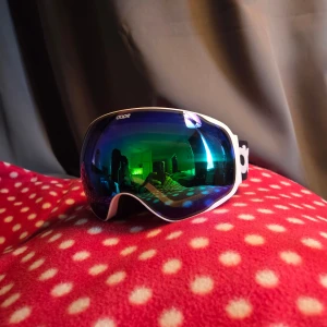 Blå skidglasögon med vit ram från Dope - Snygga skidglasögon från Dope med spegelblått glas och vit ram. Justerbart vitt band med svart logga och mjuk skumvaddering för extra komfort. Perfekta för vinterns äventyr i backen.
