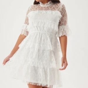 Vit spetsklänning med volanger - Superfin vit kortklänning i spets med volangdetaljer och hög hals. Klänningen har halvtransparent överdel och ärmar, samt markerad midja och flera lager i kjolen för extra volym. Perfekt för somriga tillfällen såsom skolavslutning eller stundenten!💕 Stl S i nyskick😇