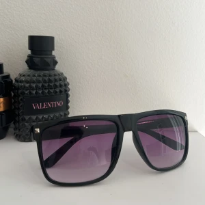 Svarta solglasögon med liten silver detalj - Stilrena solglasögon med svart, fyrkantig båge och lila tonade glas. Bågarna har små silvriga nitar i hörnen för en extra detalj. Liknar rayban boyfriends, riktigt sköna till sommarn