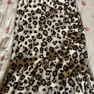Leopardmönstrad omlottkjol - Säljer en snygg leopardmönstrad omlottkjol med volangdetaljer. Kjolen har en beige bas med svarta och bruna leopardfläckar. Materialet känns mjukt och följsamt.