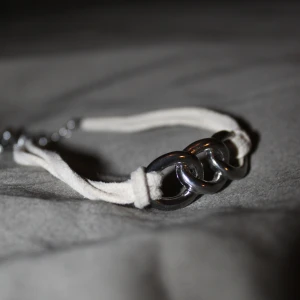 Armband Med Silverfärgade Länkar - Snyggt armband med dubbla vita mockaband och tre stora, silverfärgade metallringar framtill. Justerbar kedja i silverfärg för perfekt passform. Perfekt accessoar för att lyfta din outfit.