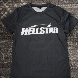 Hellstar Football Jersey Medium - Svart t-shirt från Hellstar med stort vitt tryck framtill och coolt motiv på ryggen. Klassisk passform och rund halsringning. Perfekt för dig som gillar streetwear och vill sticka ut med en unik design.