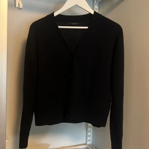 Blekblå kofta med v-ringning - En klassisk svart kofta med v-ringning och knäppning framtill. Långärmad och enkel design som passar till mycket. Perfekt basplagg i garderoben.