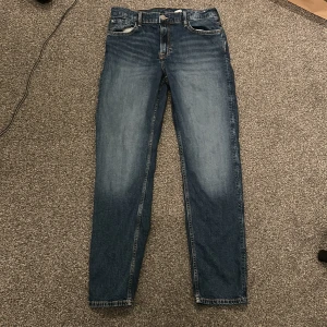 Blå raka jeans ifrån H&M - Klassiska blå jeans med raka ben och normal passform. Jeansen har fem fickor, dragkedja och knapp framtill samt ljusare partier på låren för en snygg tvättad look. Storleken är 170