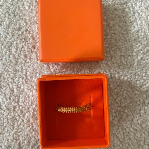 Izabel Display ring i orange strl. 58 - Säljer en snygg orange ring från Izabel Display med små glittrande stenar runt hela ringen. Perfekt accessoar för att lyfta din outfit med lite extra bling. Kommer i en orange ask.