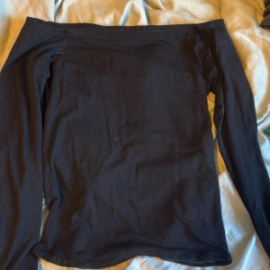 Svart offshoulder topp med långa ärmar - Säljer en svart offshoulder topp med långa ärmar. Toppen har en enkel och stilren design i mjukt material, perfekt att matcha med jeans eller kjol. Ärmarna är raka med liten slits och toppen sitter snyggt över axlarna.