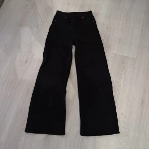 Svarta wide leg jeans från H&M - Säljer ett par svarta jeans från H&M med breda ben och klassisk femficksdesign. Byxorna har normal passform och stängs med knapp och dragkedja. Perfekta för dig som gillar en avslappnad och trendig stil.