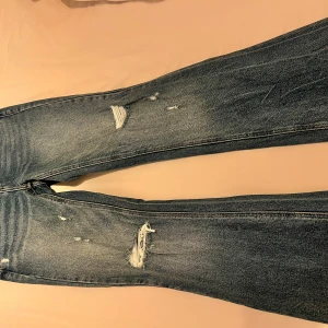 Blå bootcut jeans med slitningar - Säljer ett par blå bootcut jeans från fashion nova med slitna detaljer. Jeansen har klassisk femficksdesign och normal passform upptill som går ut i ett bootcut-snitt nertill. Perfekta för en avslappnad och trendig look.