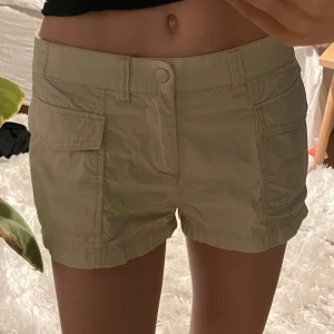 Beige cargoshorts från H&M - Snygga beige shorts från H&M Divided med normal passform och  fickor framtill. De har knapp och dragkedja samt resår baktill. Använda ett fåtal gånger.