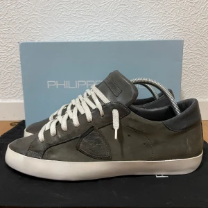 Gråa Philippe Model sneakers - Snygga Philippe Model sneakers i grått skinn med vita snören och vit platt sula. Skorna har en klassisk låg profil och diskret logga på sidan. Perfekta för en stilren och avslappnad look. Storlek 41 passar också 42. Bra skick! Nypris runt 3000 kr