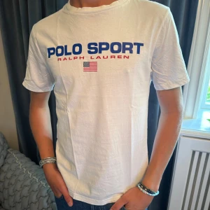Vit t-shirt från Ralph Lauren - Tja! Säljer en snygg vit t-shirt från Ralph Lauren med texten 'POLO SPORT' i blått och 'RALPH LAUREN' i rött på bröstet. Den har också en liten amerikansk flagga under texten. T shirten har aldrig använts och endast testats. Storleken är S och är true to size. Vid minsta lilla fundering tveka inte på att höra av er! Buda gärna går ner vid snabb affär!